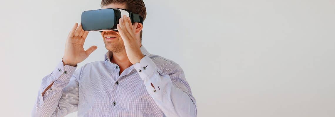 Shot of young man in virtual reality headset looking at the objects. Businessman with virtual reality goggles against grey background.